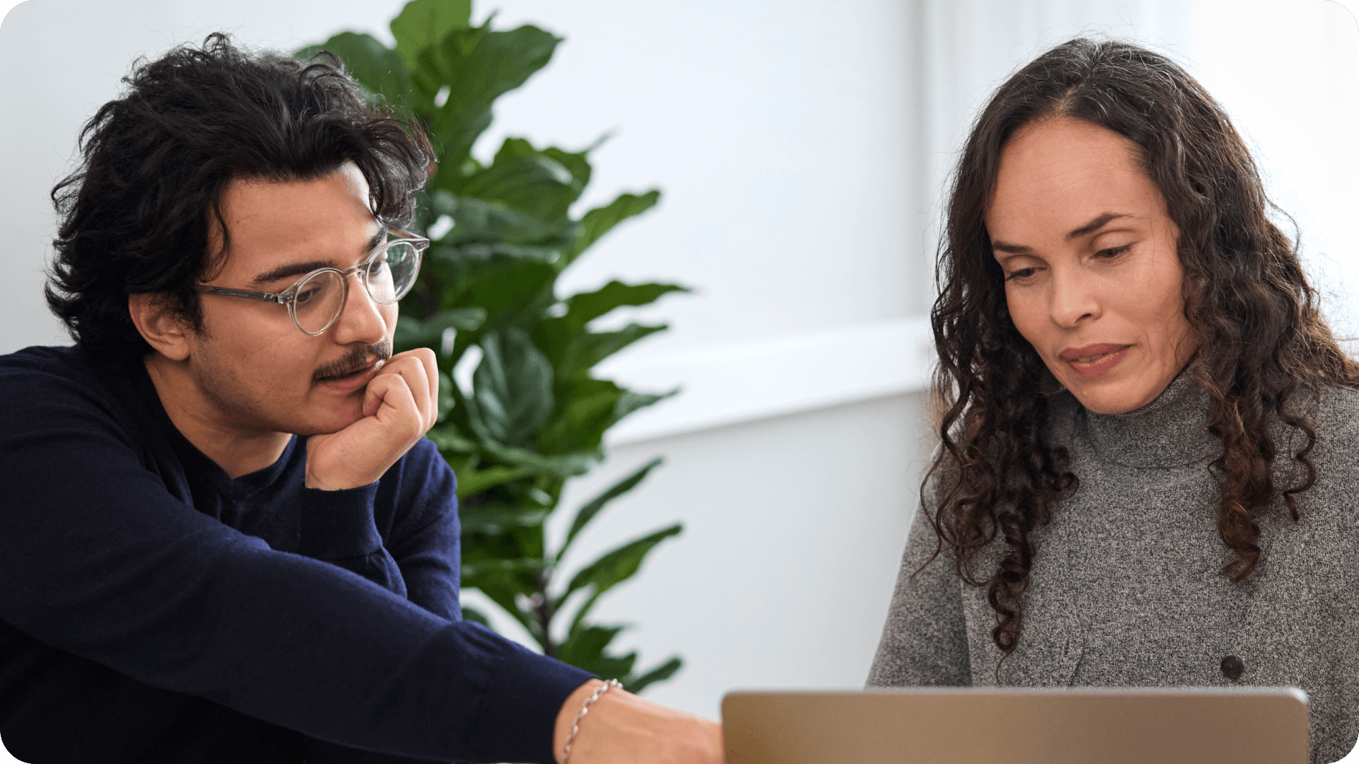 Two people sit looking at the same computer screen, the man is pointing at something.