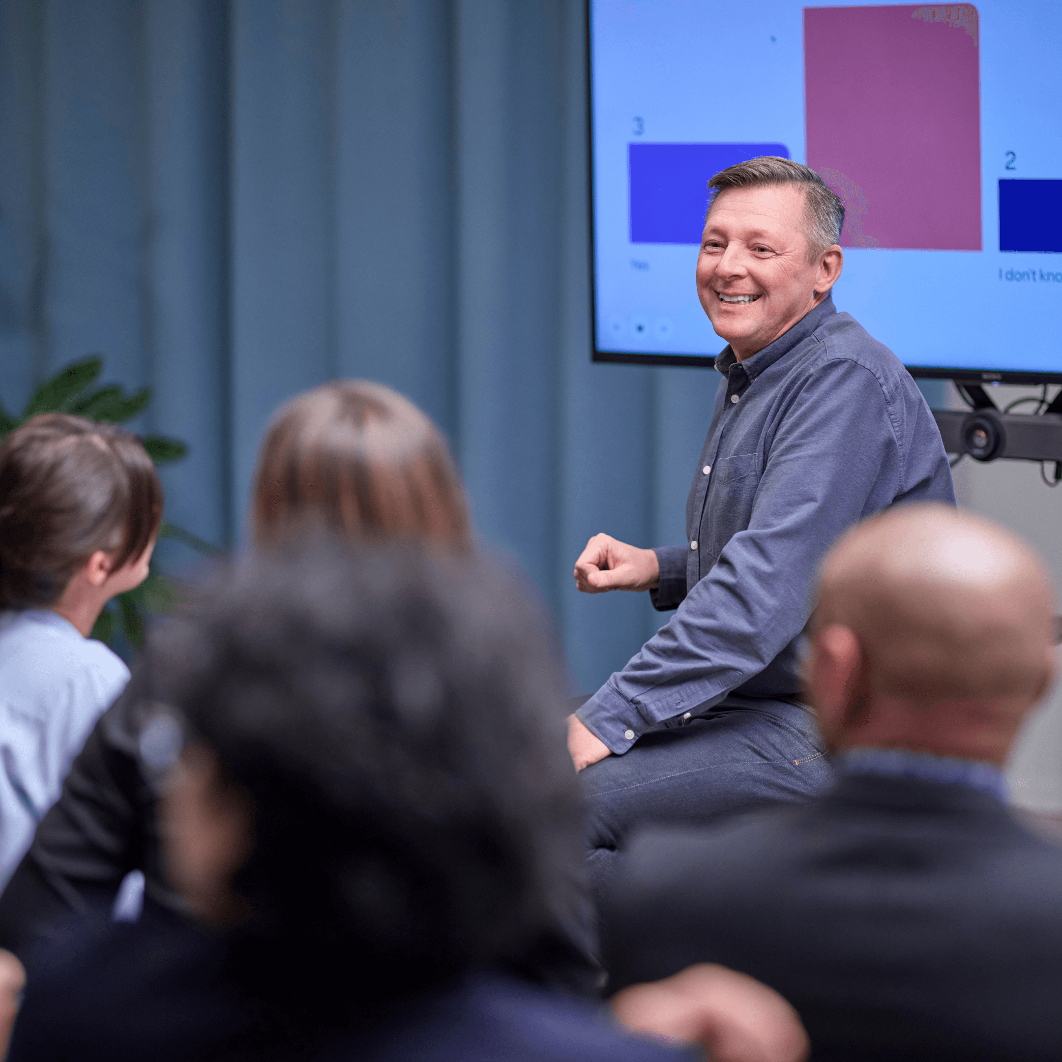 Man smiling during a presentation with an audience seated in front of him