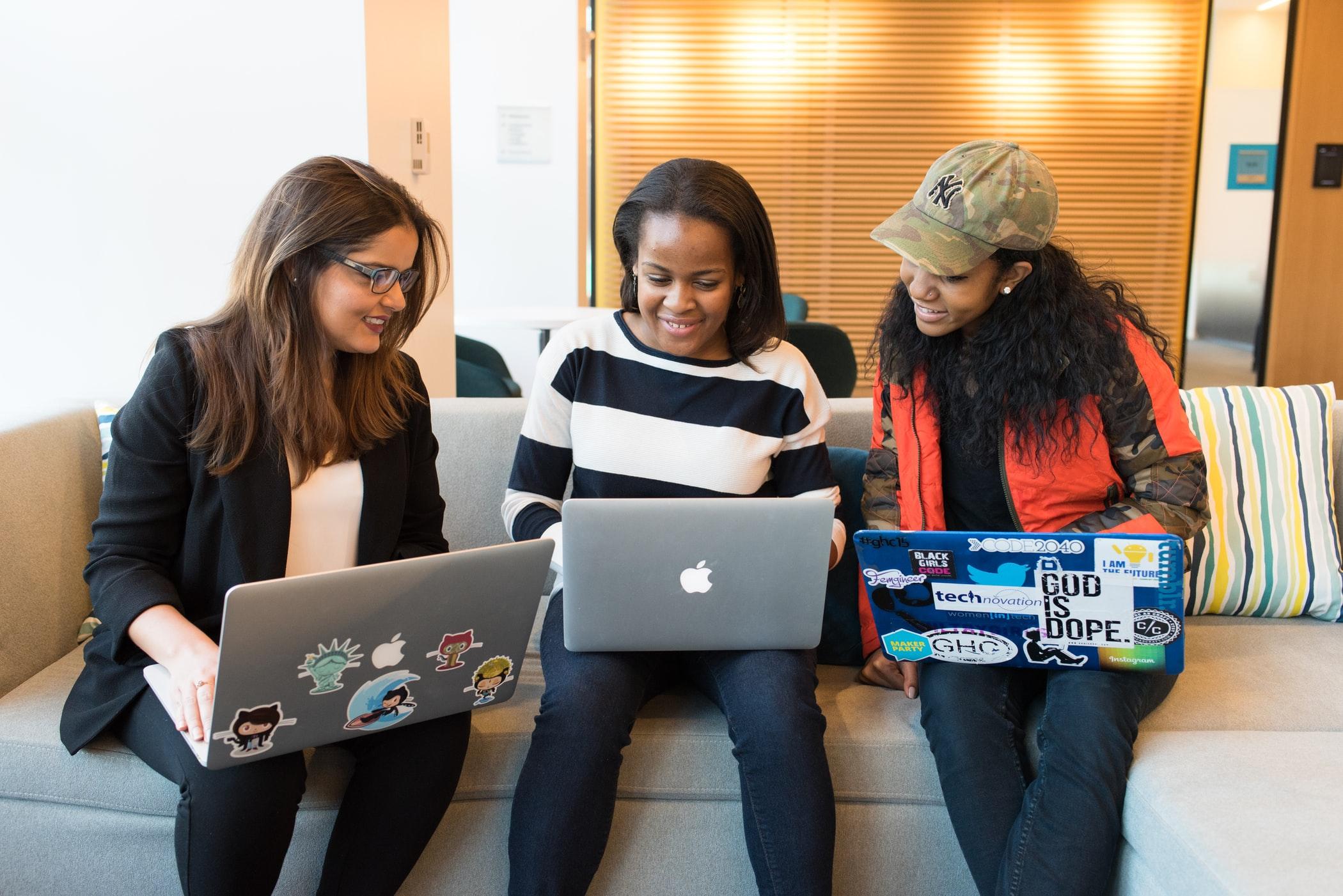 Three women with laptops sit on the sofa